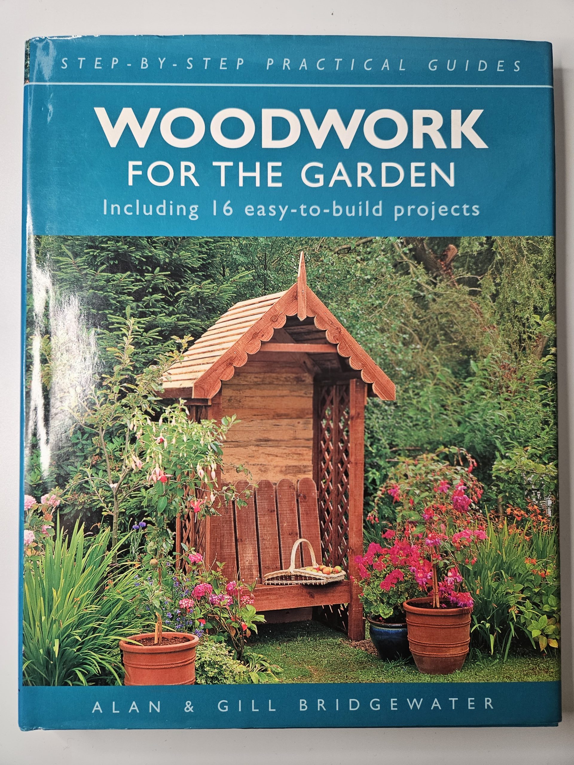 Book cover showing a lush garden with potted plants, a wooden trellis and blooming flowers against greenery, with a teal border on the right.